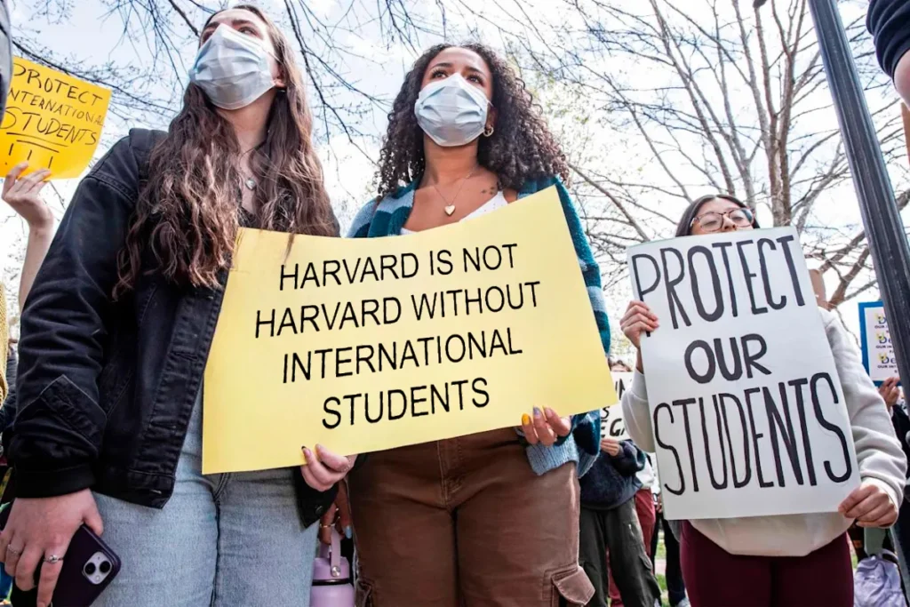 Students at Harvard University hold protest signs supporting international students and opposing the suspension of F1 visas, highlighting concerns about US student visa requirements and the impact on F1 visa holders from India.
