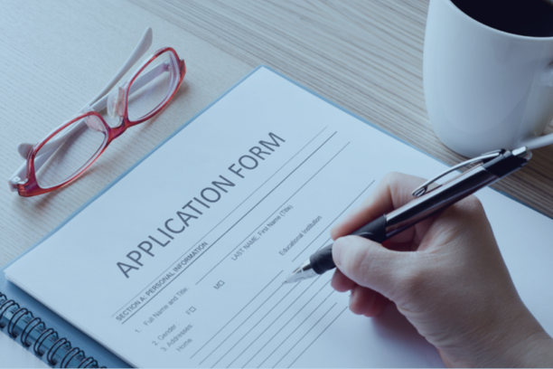 Hand filling out a visa application form with glasses and coffee cup nearby, highlighting essential documents for Singapore visa for Indians